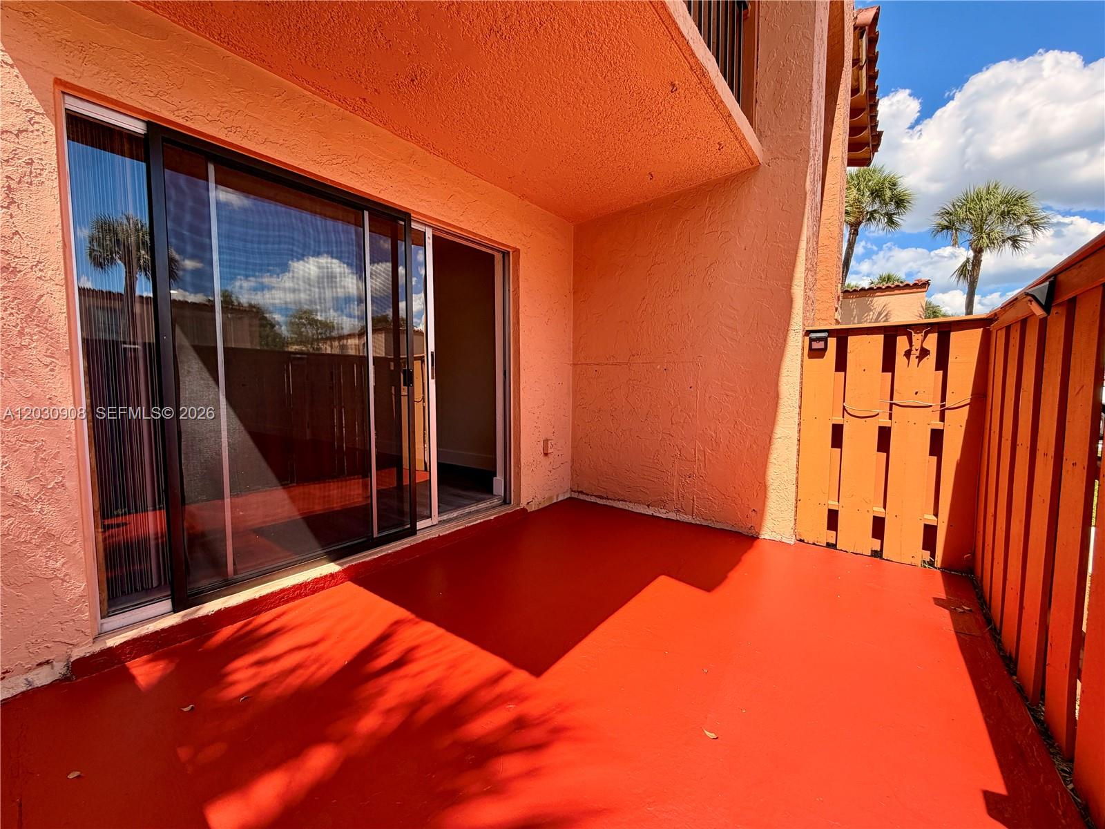A patio with red flooring, a sliding glass door, and a wooden privacy fence — MIAMI LAKES, FL