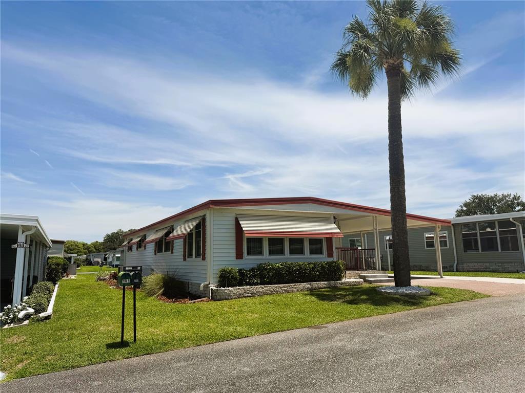 A single-story mobile home with a palm tree and a carport under a blue sky — 101 MARIGOLD STREET, LEESBURG, FL