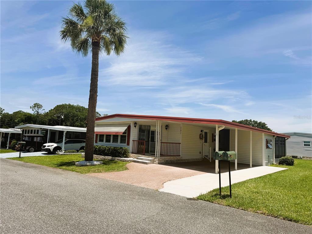 A single-story manufactured home with a carport, red roof, and a palm tree in front — 101 MARIGOLD STREET, LEESBURG, FL