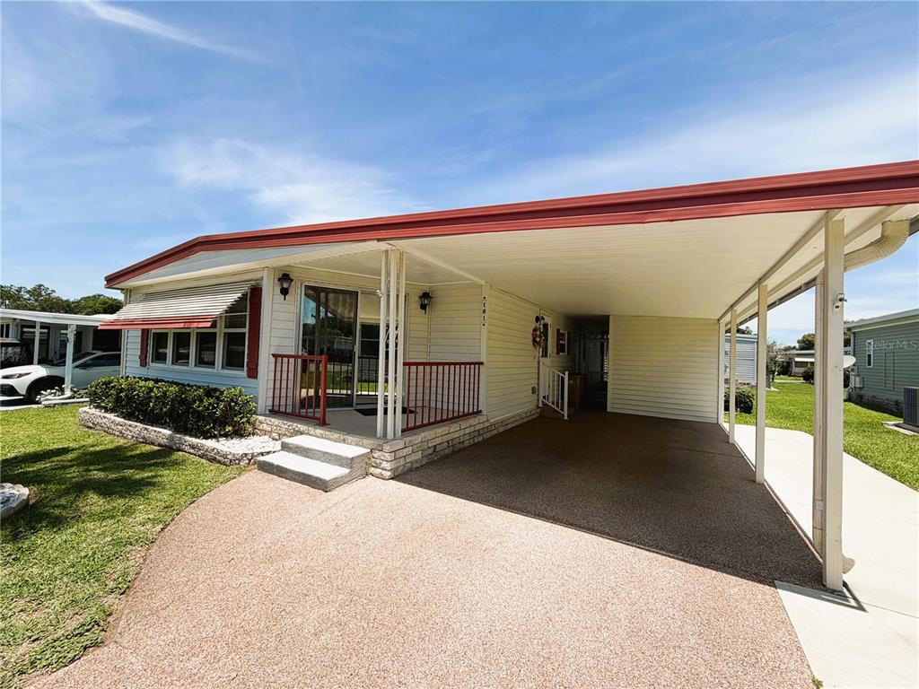 A single-story manufactured home features a red roof, a covered carport, and a front porch — 101 MARIGOLD STREET, LEESBURG, FL