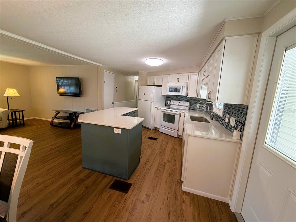 A kitchen with white cabinets, a gray island, and stainless steel appliances opens to a living area — 101 MARIGOLD STREET, LEESBURG, FL