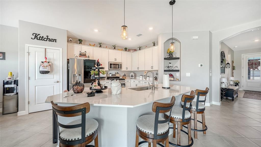 A kitchen features white cabinetry, a large central island with bar seating, and pendant lighting — 4971 OYSTER PEARL STREET, BRADENTON, FL