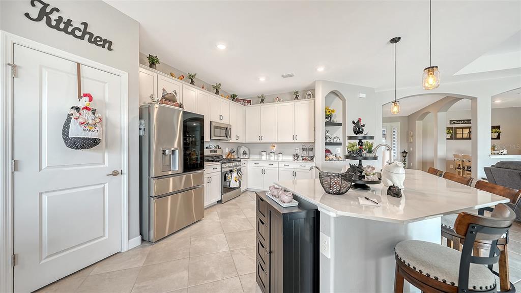 A kitchen features white cabinetry, stainless steel appliances, a marble-topped island, and tile flooring — 4971 OYSTER PEARL STREET, BRADENTON, FL