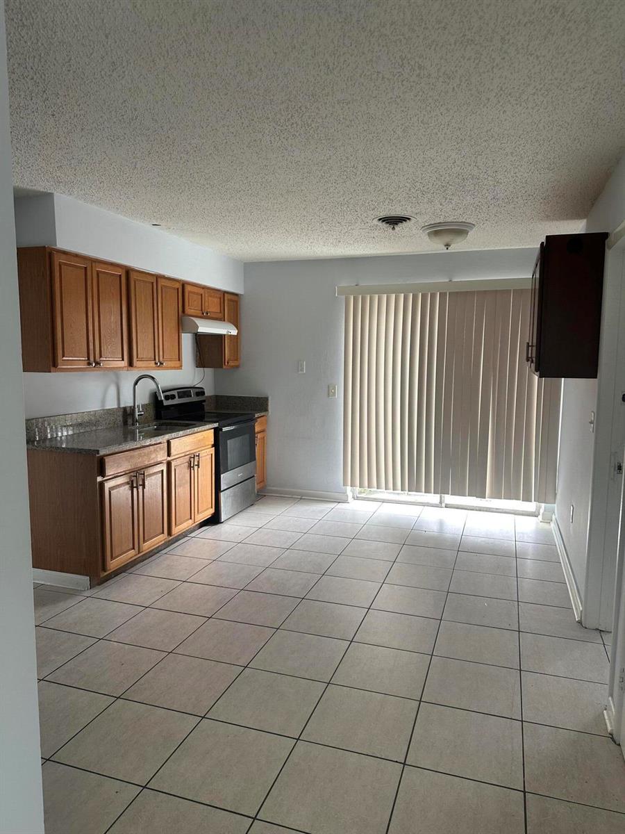 A kitchen with wood cabinets, granite countertops, tile flooring, and a sliding glass door — 3194 Prince Drive # 3196, Lake Worth FL 33461, LAKE WORTH, FL