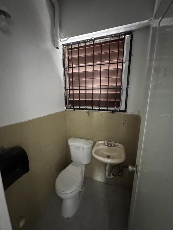 A small bathroom features a white toilet, a wall-mounted sink, and a barred window — 17 NC PERAL UNIT 1B, MAYAGUEZ, PR