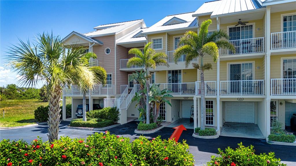 An exterior view of a multi-story townhouse complex with palm trees and a ground-level garage — 3273 MANGROVE POINT DRIVE, RUSKIN, FL
