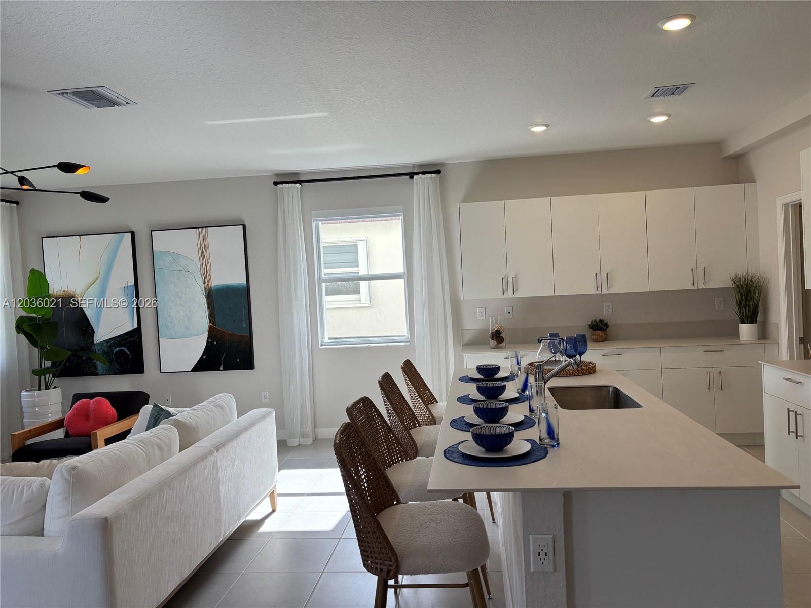 A kitchen with white cabinets and an island features four chairs and abstract wall art — 2342 SE 30th St, Homestead FL 33035, HOMESTEAD, FL