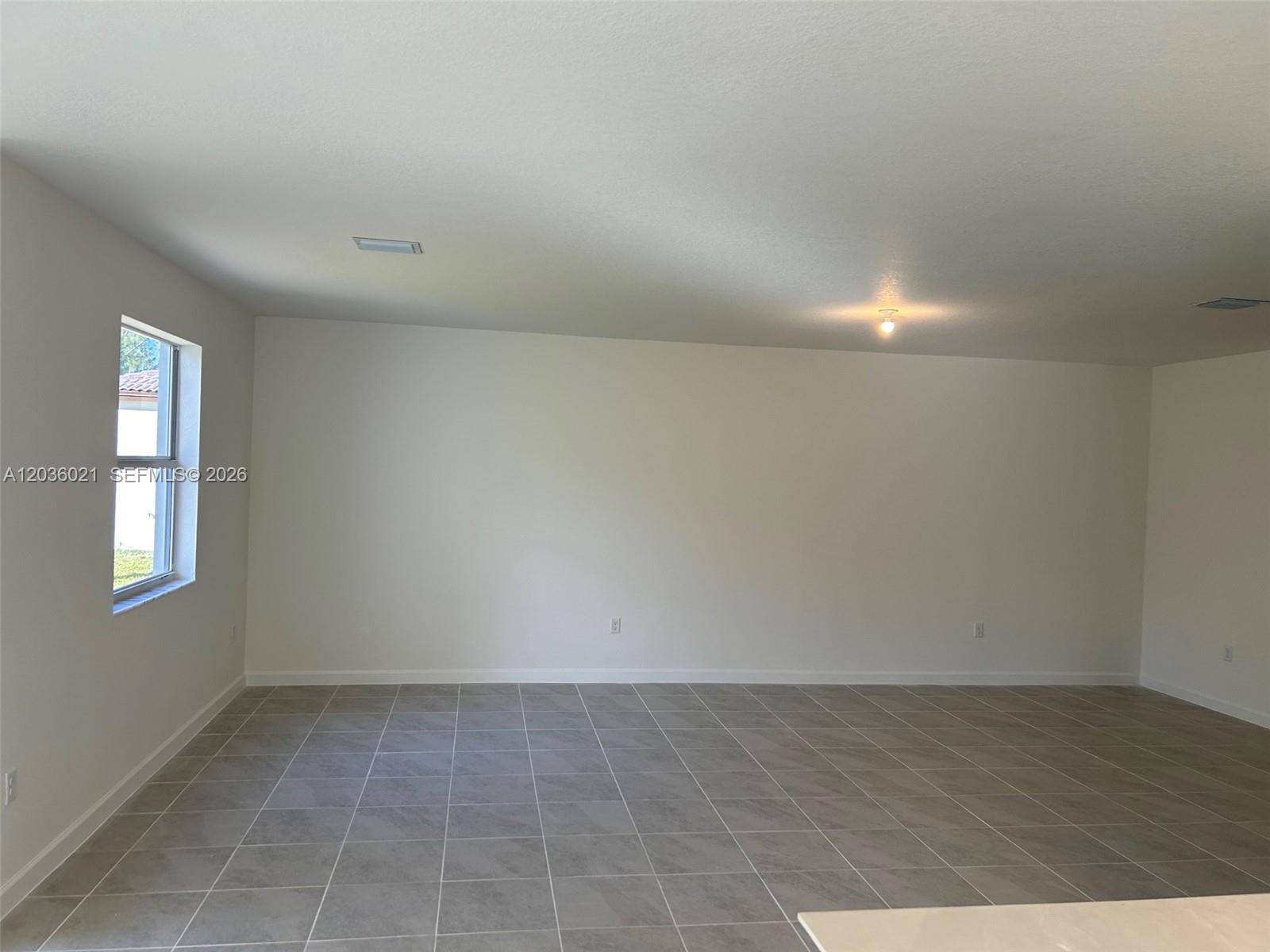 An empty room features white walls, gray tile flooring, and a single window — 2342 SE 30th St, Homestead FL 33035, HOMESTEAD, FL