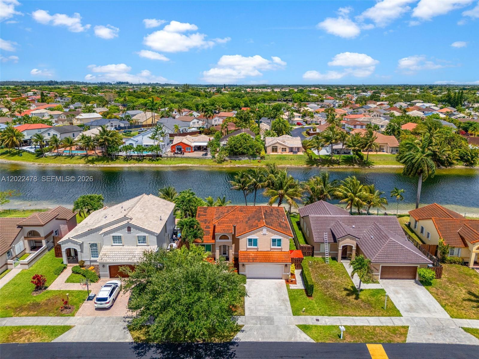 An aerial view shows three suburban houses with tiled roofs situated along a canal — 15891 SW 84th St, Miami FL 33193, MIAMI, FL