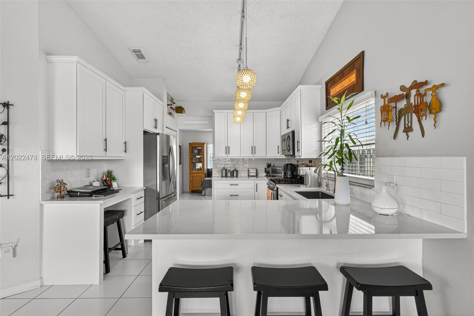 A modern kitchen features white cabinetry, quartz countertops, a breakfast bar, and three black stools — 15891 SW 84th St, Miami FL 33193, MIAMI, FL