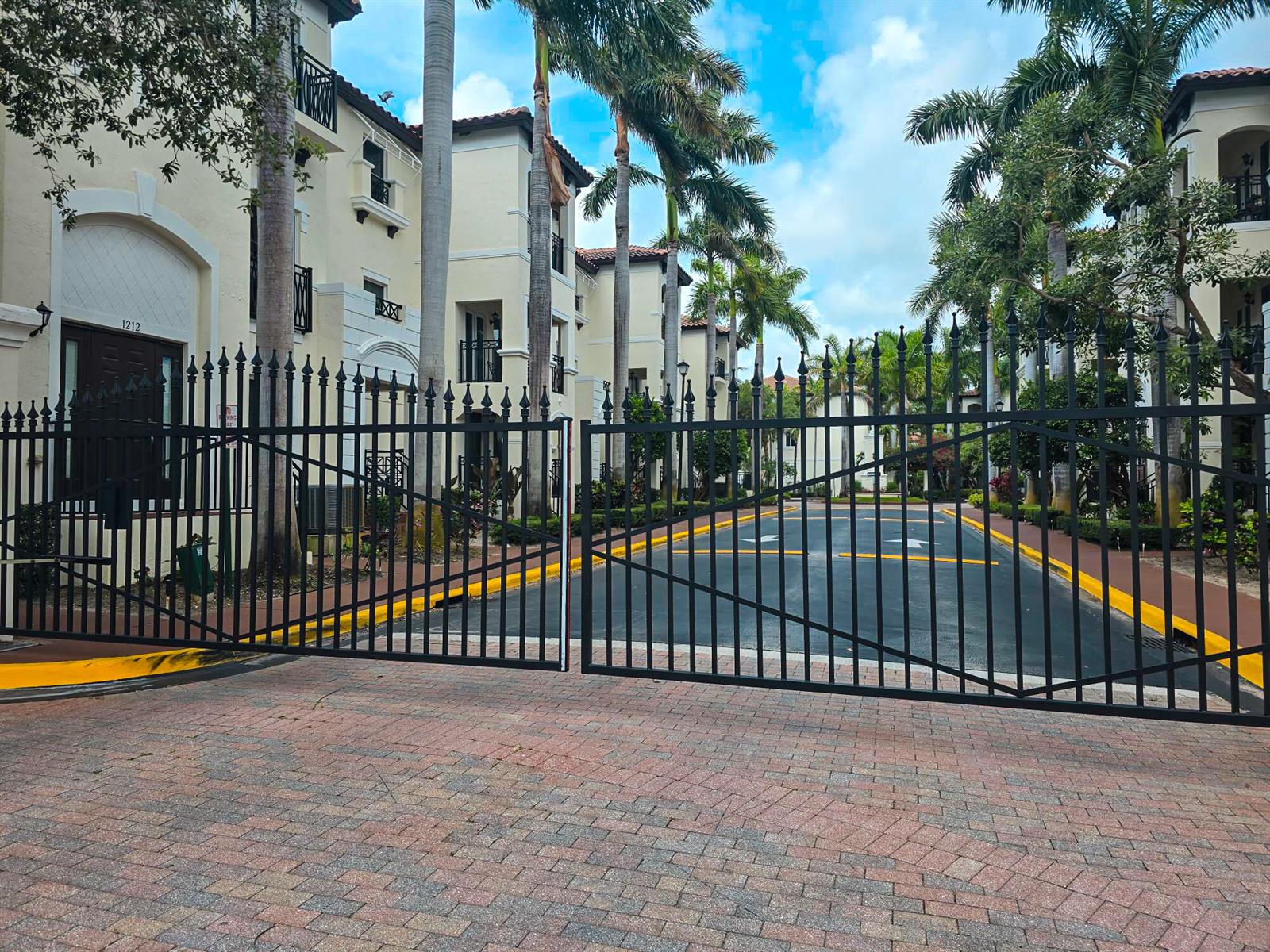 A black metal gate stands at the entrance of a multi-story apartment complex with palm trees — 1602 Coastal Bay Boulevard, Boynton Beach FL 33435, BOYNTON BEACH, FL
