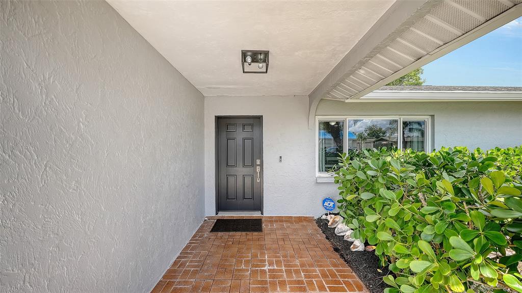 A gray front door with a brick porch and a large green hedge — 972 LEEWARD ROAD, VENICE, FL