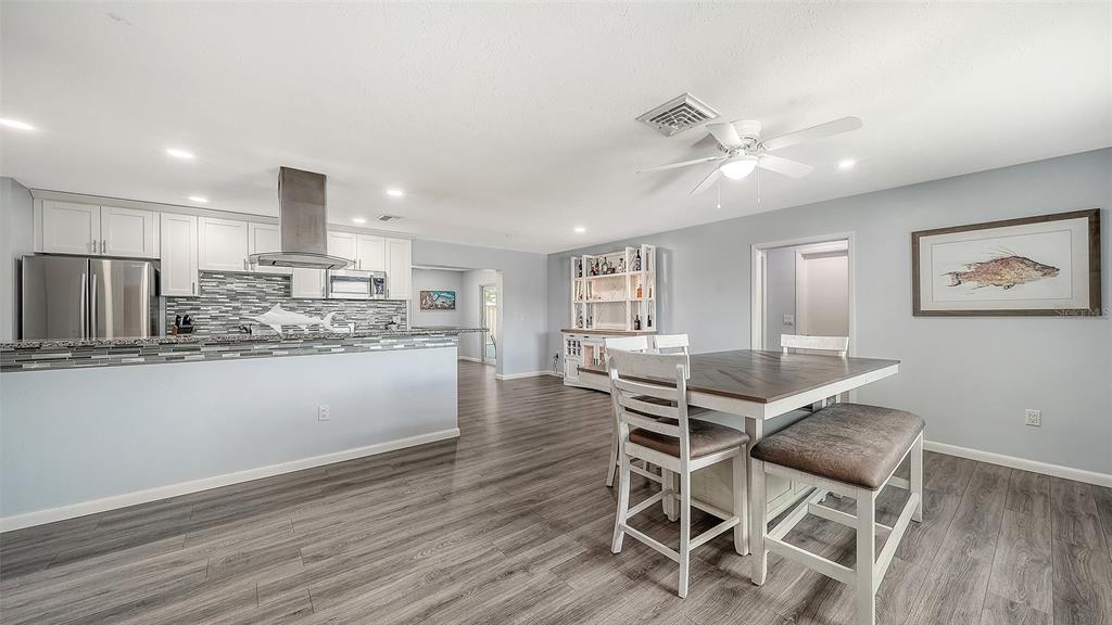 A kitchen and dining area with white cabinets, gray wood flooring, and a ceiling fan — 972 LEEWARD ROAD, VENICE, FL