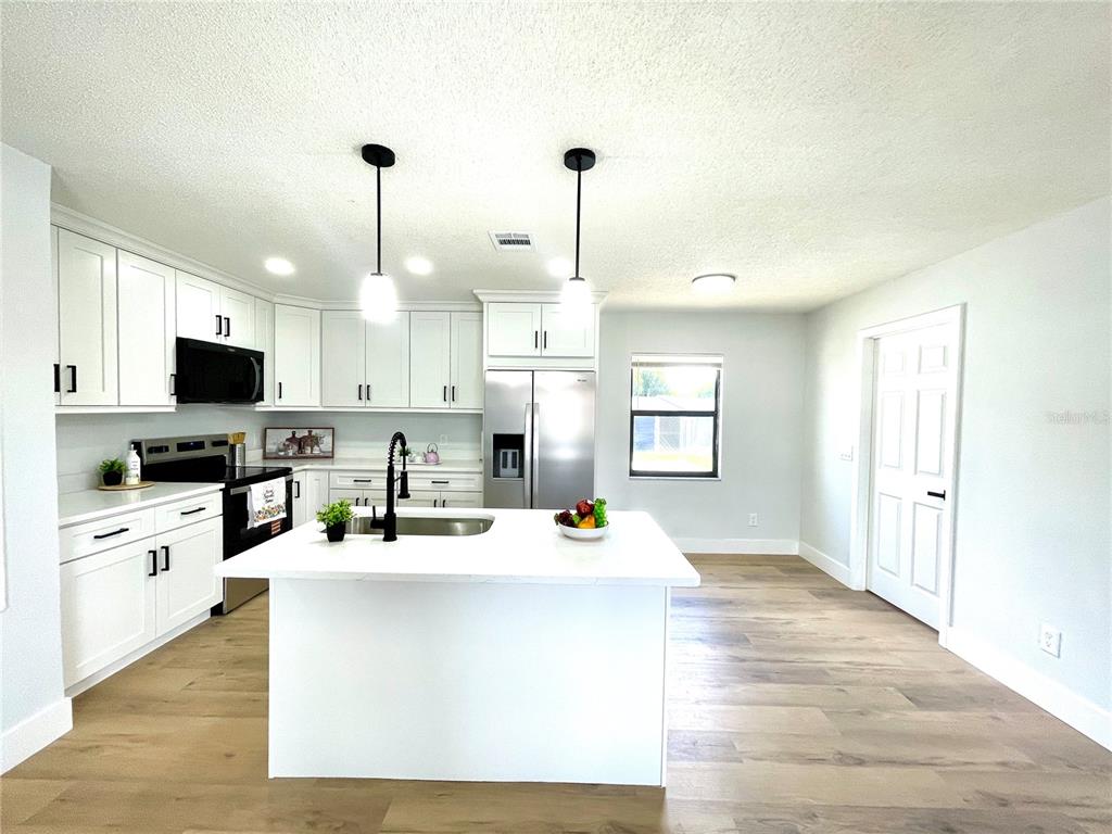 A modern kitchen features white cabinetry, a central island with a sink, and light wood flooring — 2952 MORRIS DRIVE, BARTOW, FL