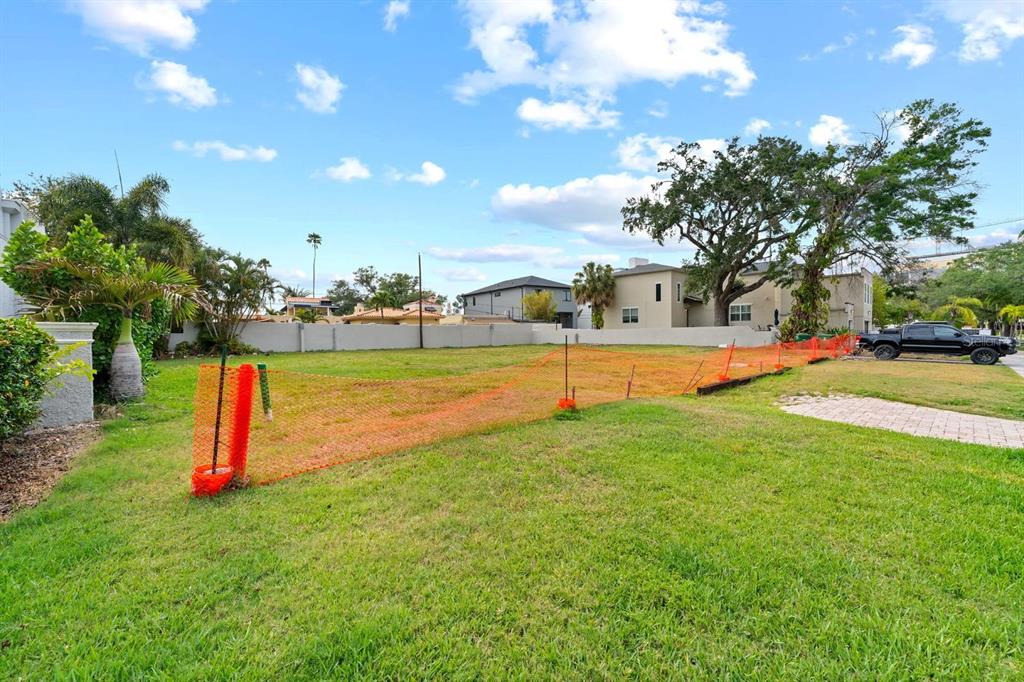 A vacant grassy lot is enclosed by orange construction fencing under a blue sky — 32 AEGEAN AVENUE, TAMPA, FL