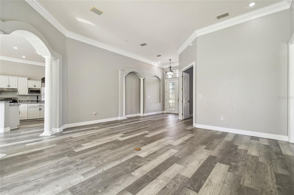 An open-concept living area features gray wood-look flooring, arched wall niches, and a white kitchen — 6644 COUNTRY CLUB ROAD, WESLEY CHAPEL, FL