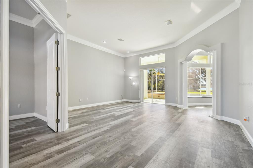 A spacious living room with gray wood-look flooring, high ceilings, and a sliding glass door — 6644 COUNTRY CLUB ROAD, WESLEY CHAPEL, FL