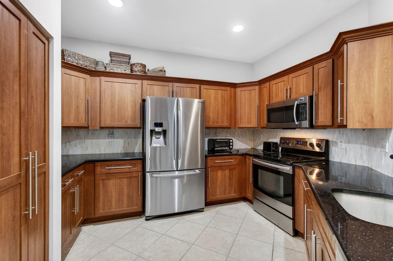 A kitchen features wood cabinets, black granite countertops, stainless steel appliances, and tile flooring — 12636 Via Ravenna, Boynton Beach FL 33436, BOYNTON BEACH, FL