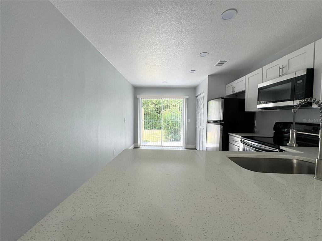 A kitchen with white cabinets, quartz countertops, and a sliding glass door to the backyard — 440 S HILL AVENUE, DELAND, FL