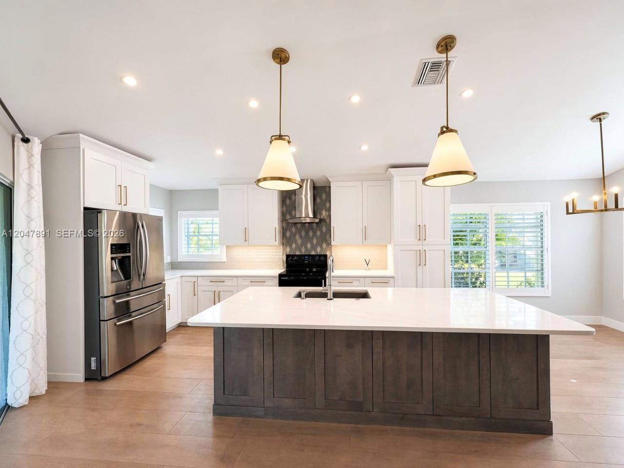 A modern kitchen features white cabinetry, a dark wood island, and stainless steel appliances — ESTERO, FL