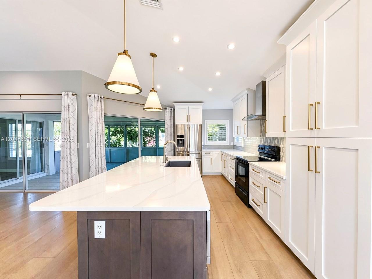 A modern kitchen features a large white quartz island, dark cabinetry, and stainless steel appliances — ESTERO, FL