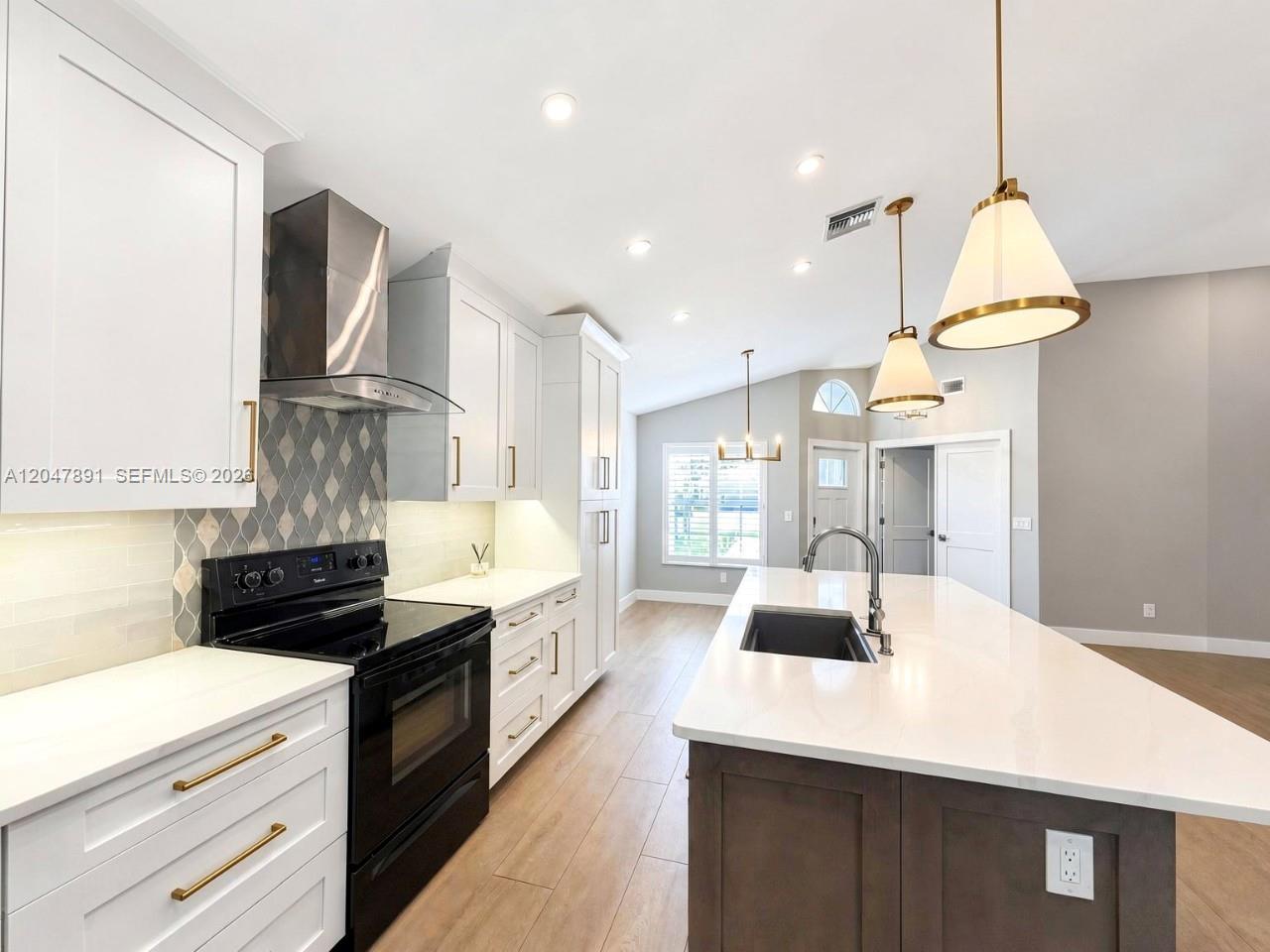 A modern kitchen features white cabinets, a dark island, stainless appliances, and pendant lighting — ESTERO, FL