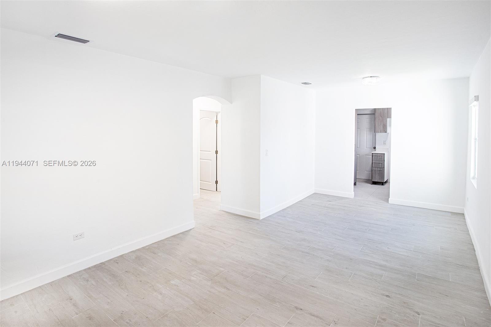 An empty room features white walls, light wood-look tile flooring, and two arched doorways — 2620 SW 9th St, Miami FL 33135, MIAMI, FL