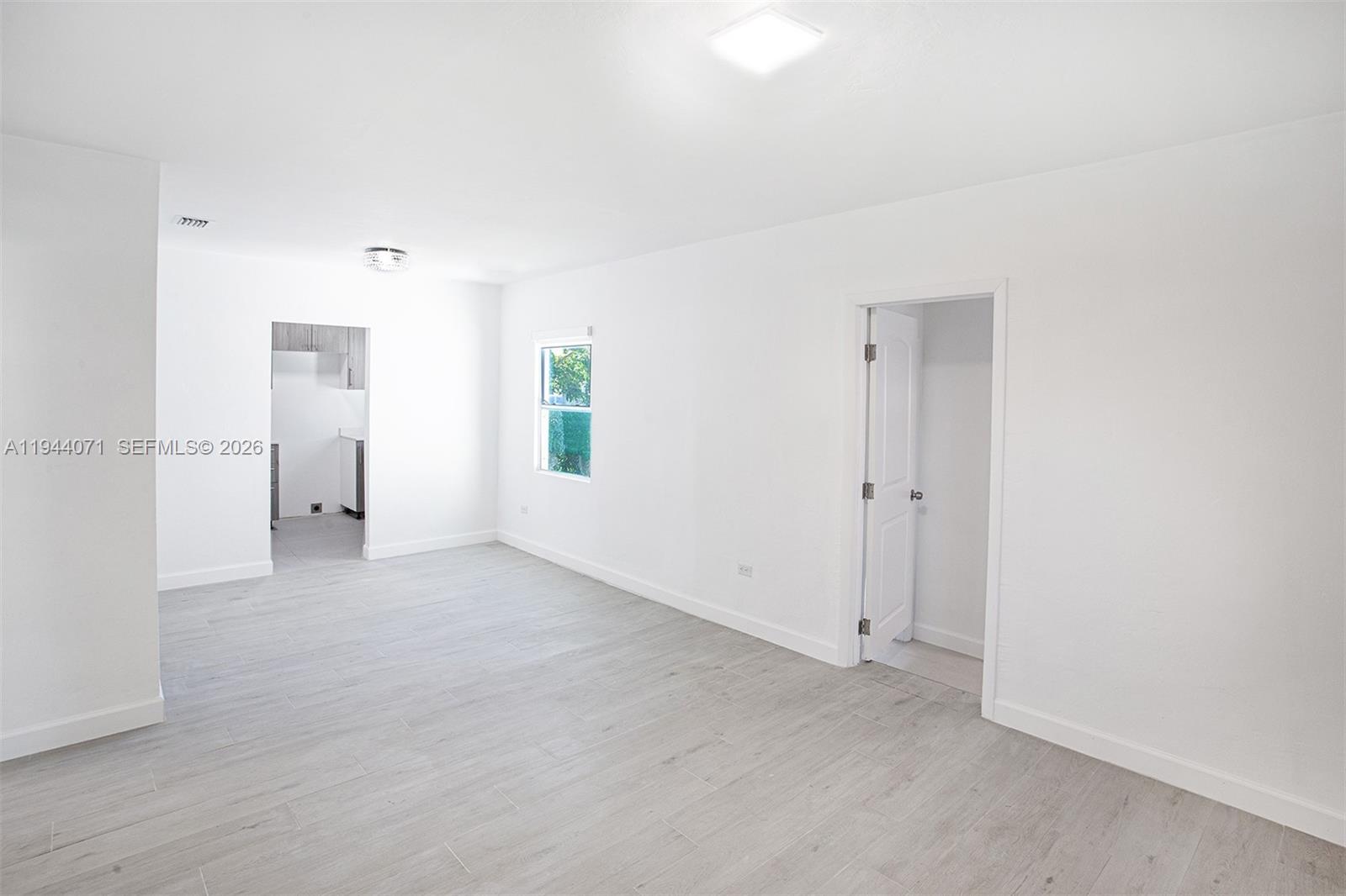 A bright, minimalist room features light gray wood-look flooring, white walls, and a doorway — 2620 SW 9th St, Miami FL 33135, MIAMI, FL