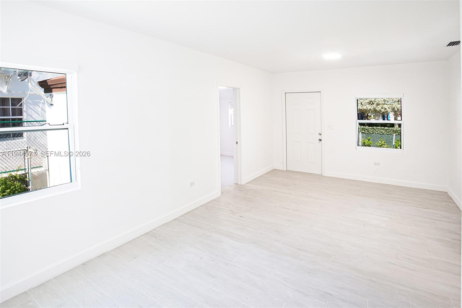 A bright, empty room features white walls, light wood-look tile flooring, and two windows — 2620 SW 9th St, Miami FL 33135, MIAMI, FL
