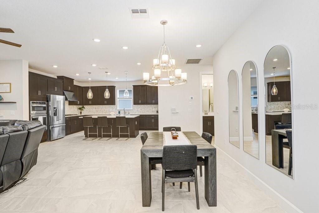 A dining area with a wooden table and chandelier opens into a kitchen with dark cabinetry — 11417 TRIVIO TERRACE, PALMETTO, FL