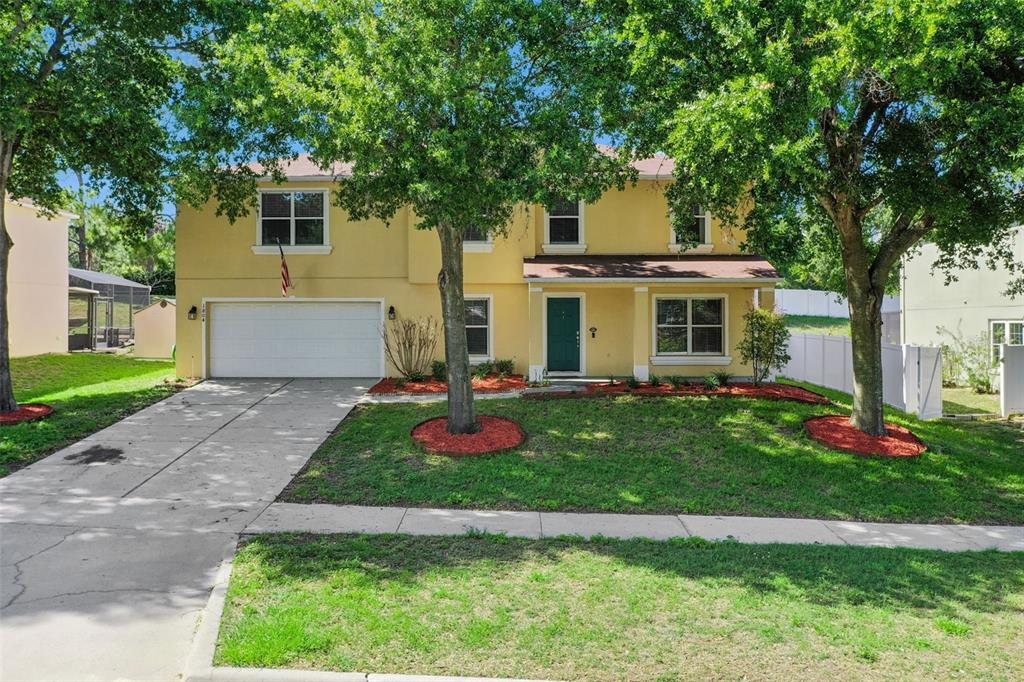 A two-story yellow house with a two-car garage, a green front door, and mature trees — 1804 VALE DRIVE, CLERMONT, FL