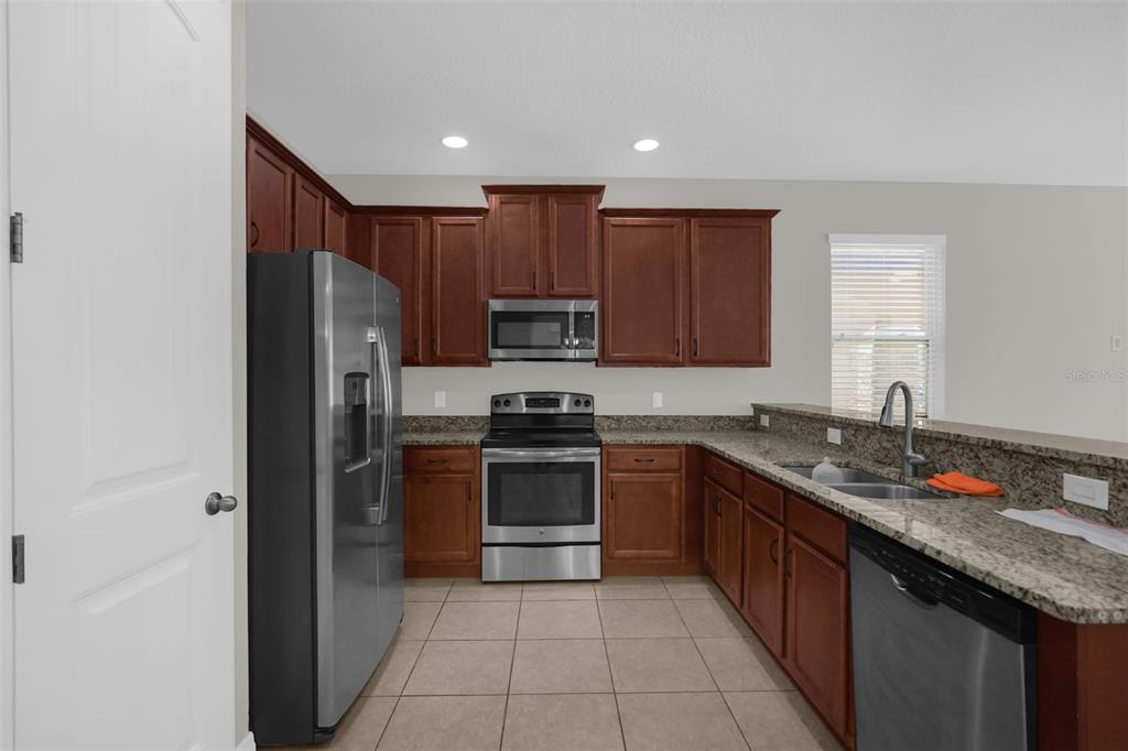 A kitchen features dark wood cabinets, granite countertops, stainless steel appliances, and tile flooring — 13845 BRIDGEWATER CROSSINGS BLVD, WINDERMERE, FL