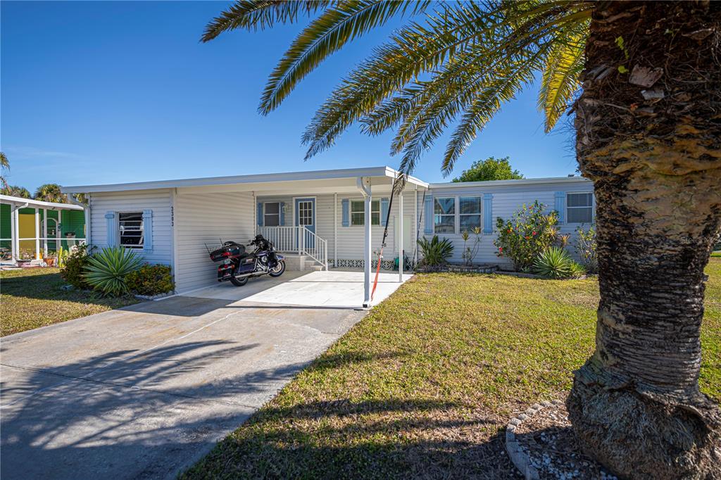 A single-story manufactured home with a carport, a motorcycle, and a large palm tree — 3303 BLUE JAY LANE, ENGLEWOOD, FL