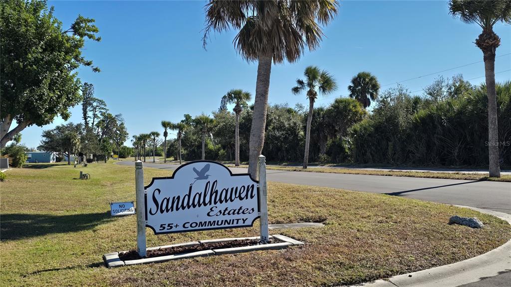 A sign for Sandalhaven Estates 55+ Community stands near a road with palm trees — 3303 BLUE JAY LANE, ENGLEWOOD, FL