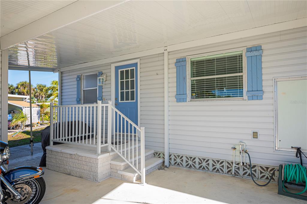 A light gray mobile home exterior features a blue front door, shutters, and a carport — 3303 BLUE JAY LANE, ENGLEWOOD, FL