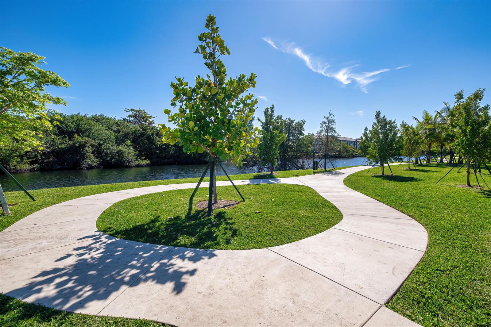A concrete path curves through a grassy park area with young trees beside a lake — 2000 Stirling Road # 106, Hollywood FL 33020, HOLLYWOOD, FL