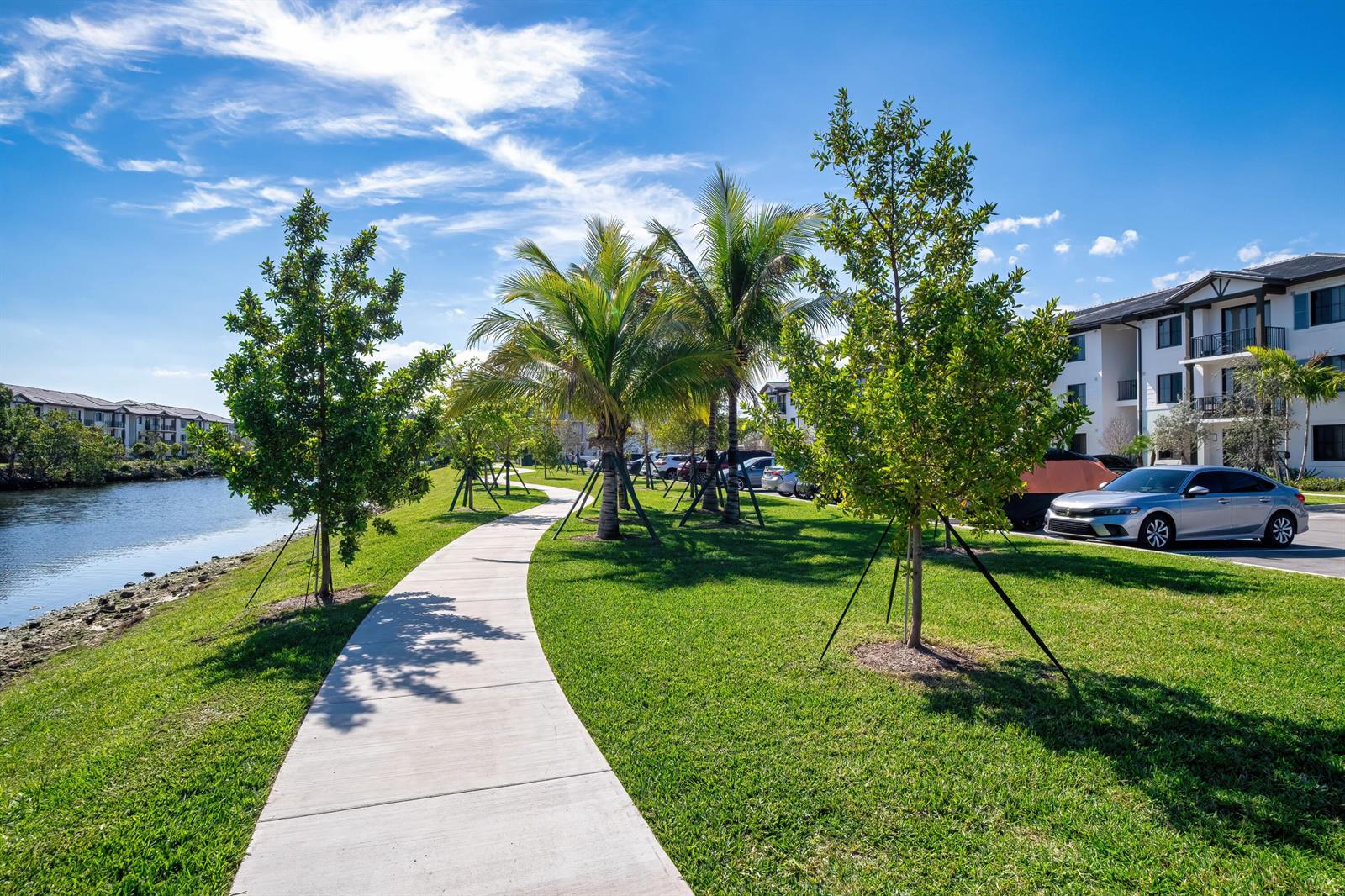 A concrete walking path winds through a grassy area with trees beside a canal — 2000 Stirling Road # 106, Hollywood FL 33020, HOLLYWOOD, FL