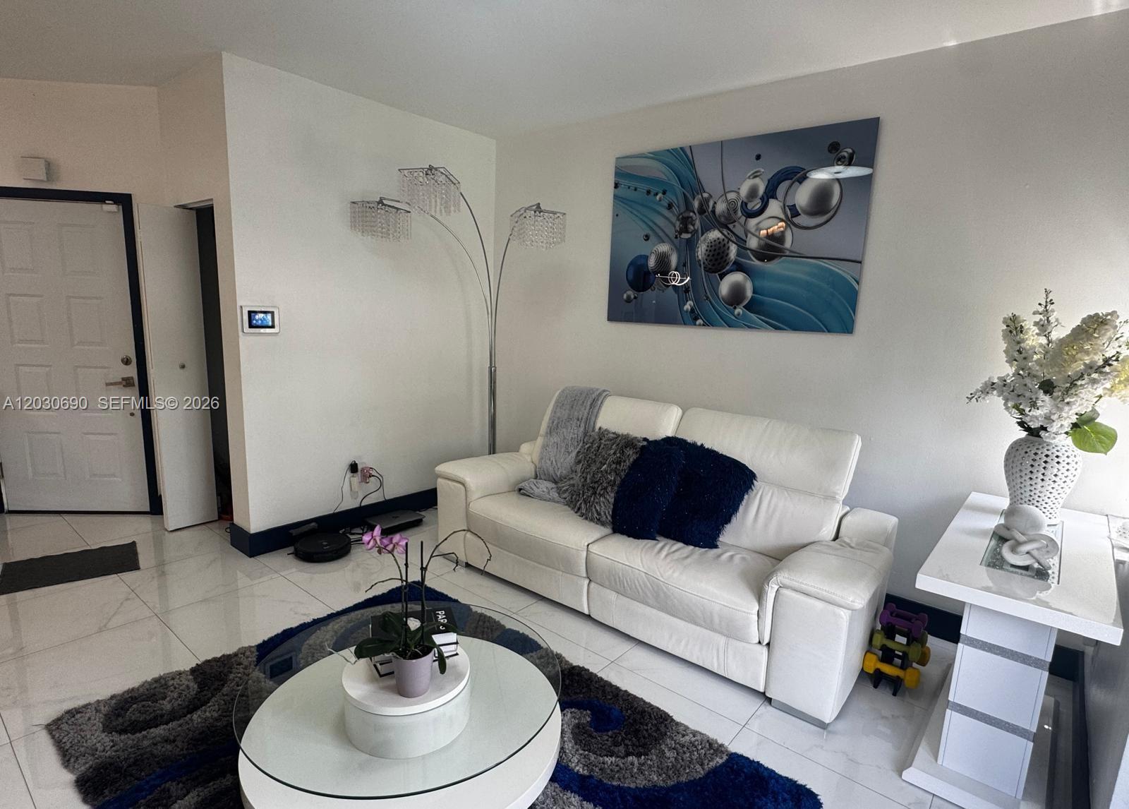 A living room features a white sofa, a glass coffee table, and abstract wall art — 18306 NW 68th Ave # A, Hialeah FL 33015, HIALEAH, FL