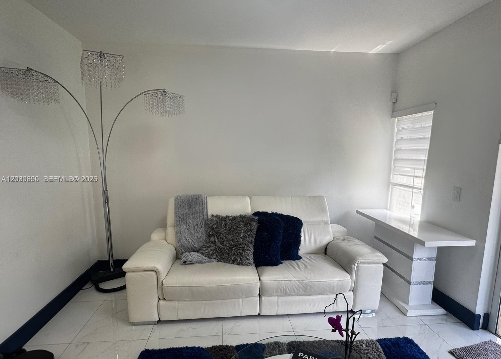 A white leather loveseat sits in a room with a crystal floor lamp and tile flooring — 18306 NW 68th Ave # A, Hialeah FL 33015, HIALEAH, FL