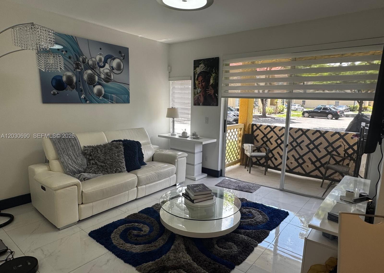 A living room features a white sofa, a glass coffee table, and a sliding door — 18306 NW 68th Ave # A, Hialeah FL 33015, HIALEAH, FL