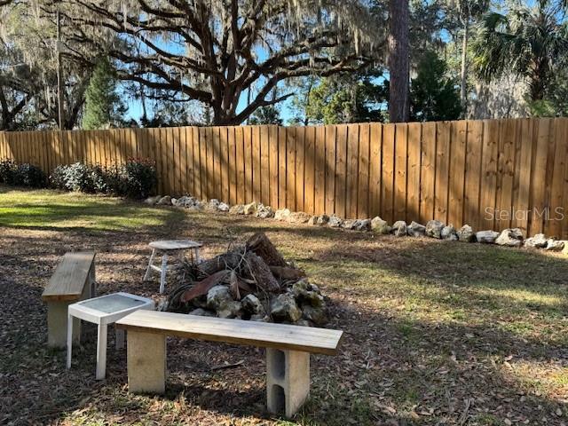 A backyard features a wooden fence, a stone fire pit, and two benches on a lawn — 15050 NE 113TH COURT, FORT MC COY, FL