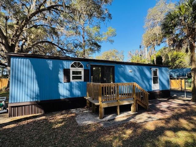 A blue mobile home features a wooden deck and a brown skirt in a yard — 15050 NE 113TH COURT, FORT MC COY, FL