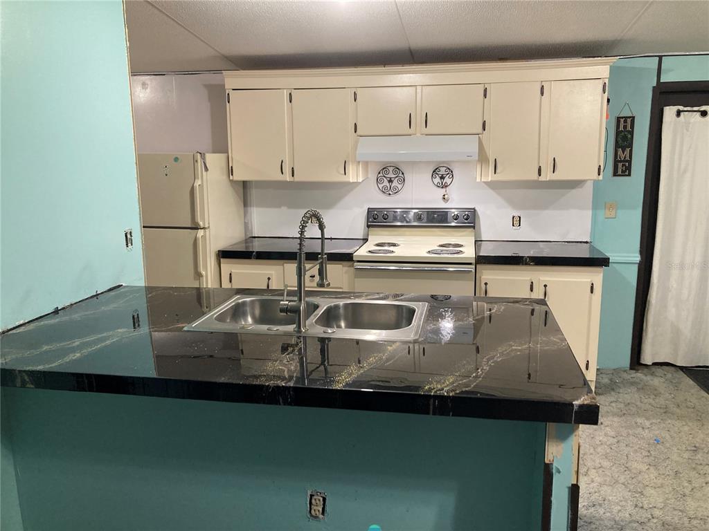 A kitchen features black countertops, cream-colored cabinets, a stainless steel sink, and a white stove — 15050 NE 113TH COURT, FORT MC COY, FL