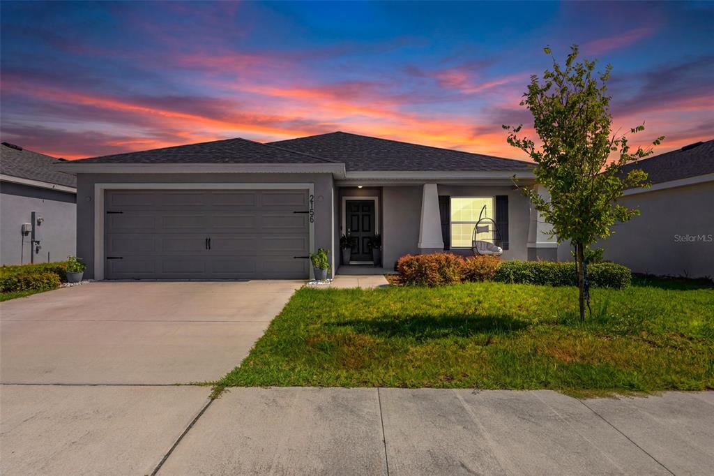 A single-story house with a gray garage, dark front door, and lawn at sunset — 2156 DESERT ROSE DRIVE, DAVENPORT, FL