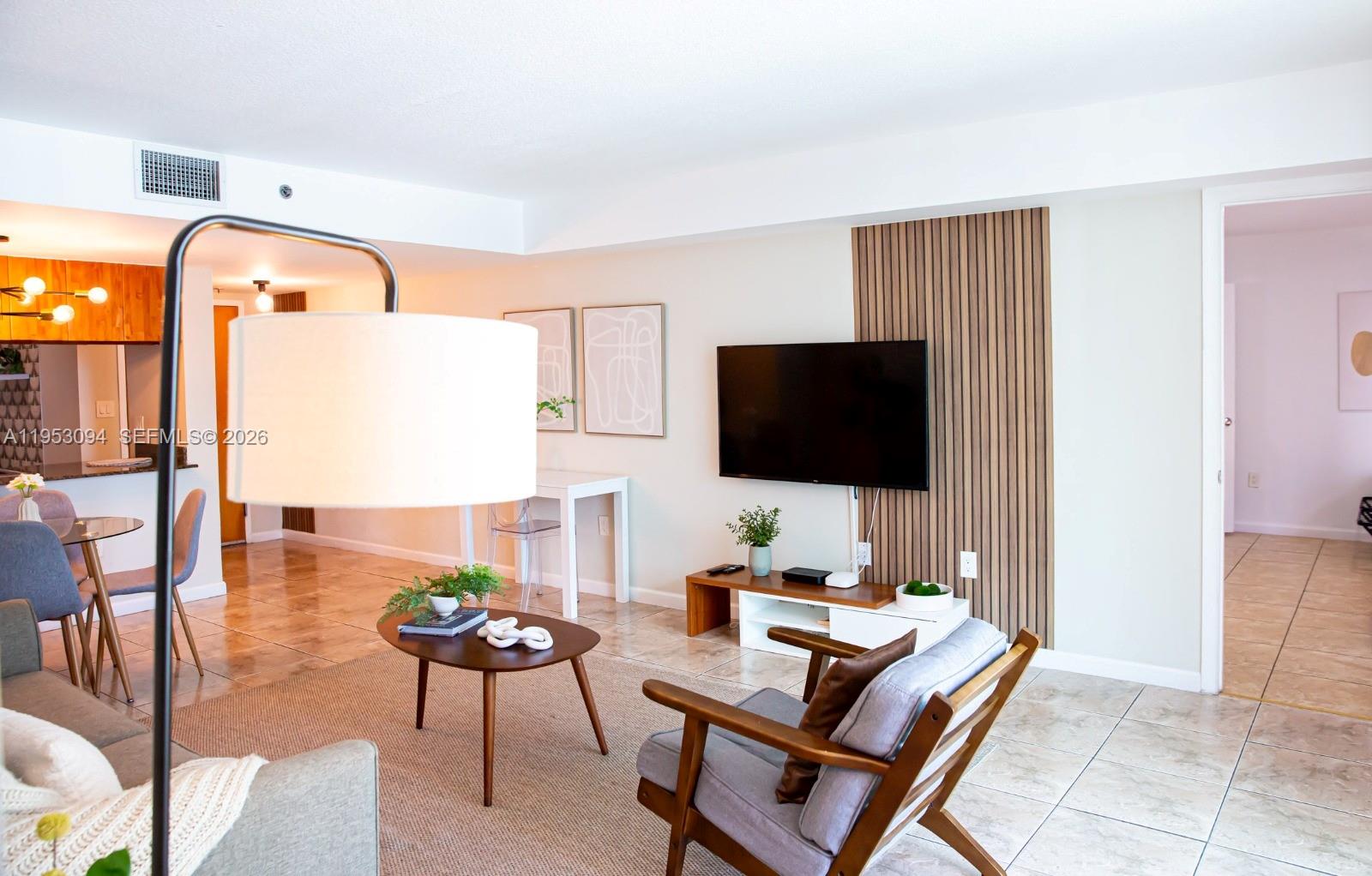 A living room features a wall-mounted television on a wood-slat accent panel and tile flooring — 1200 Brickell Bay Dr # 3215, Miami FL 33131, MIAMI, FL