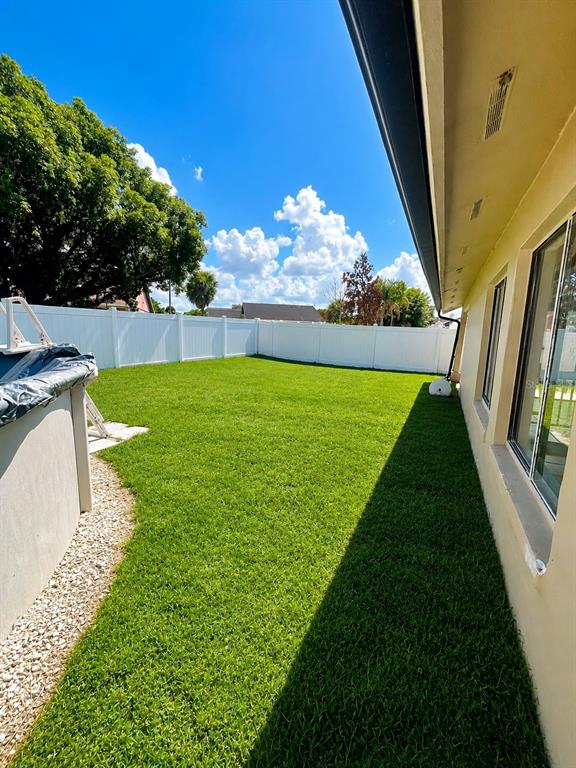 A grassy backyard features a white vinyl fence, a partial pool, and a house exterior — 17 S FLAG DRIVE, KISSIMMEE, FL