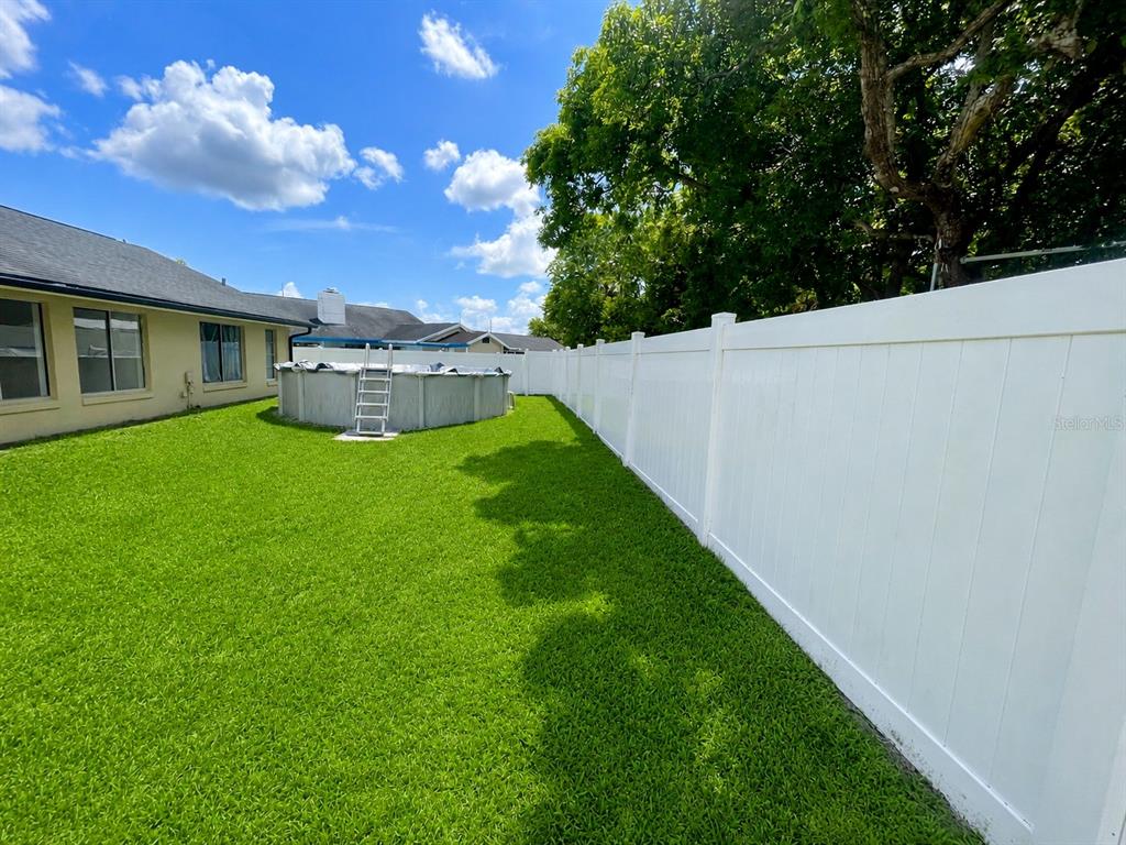 A backyard features a green lawn, a white vinyl fence, and an above-ground swimming pool — 17 S FLAG DRIVE, KISSIMMEE, FL