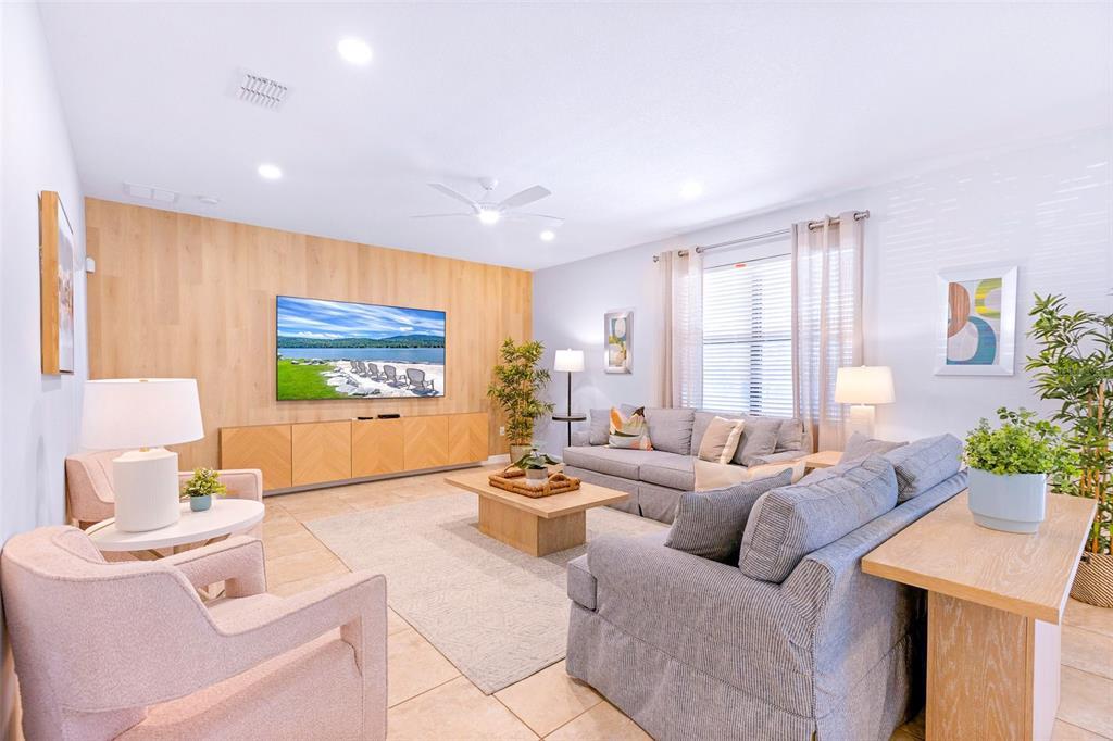 A living room features a light wood accent wall, a television, and gray seating — 9023 SHADOW MOUNTAIN STREET, DAVENPORT, FL