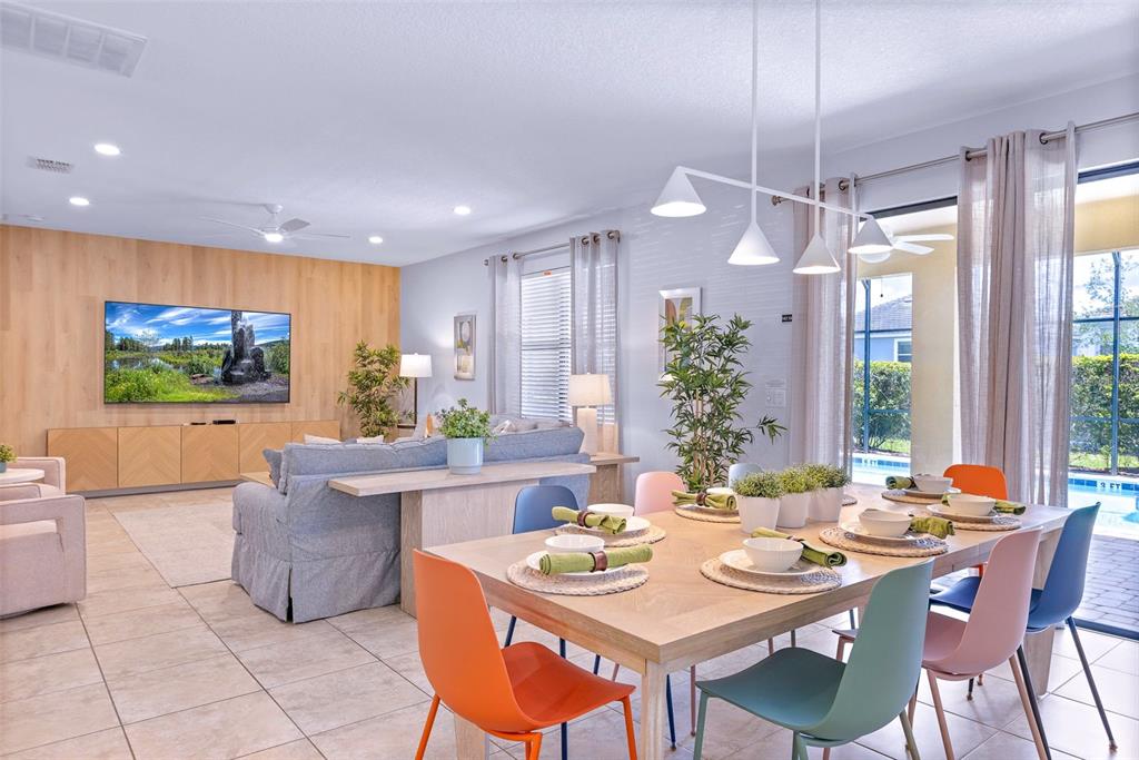 A dining area with colorful chairs sits in front of a living room with wood-paneled walls — 9023 SHADOW MOUNTAIN STREET, DAVENPORT, FL