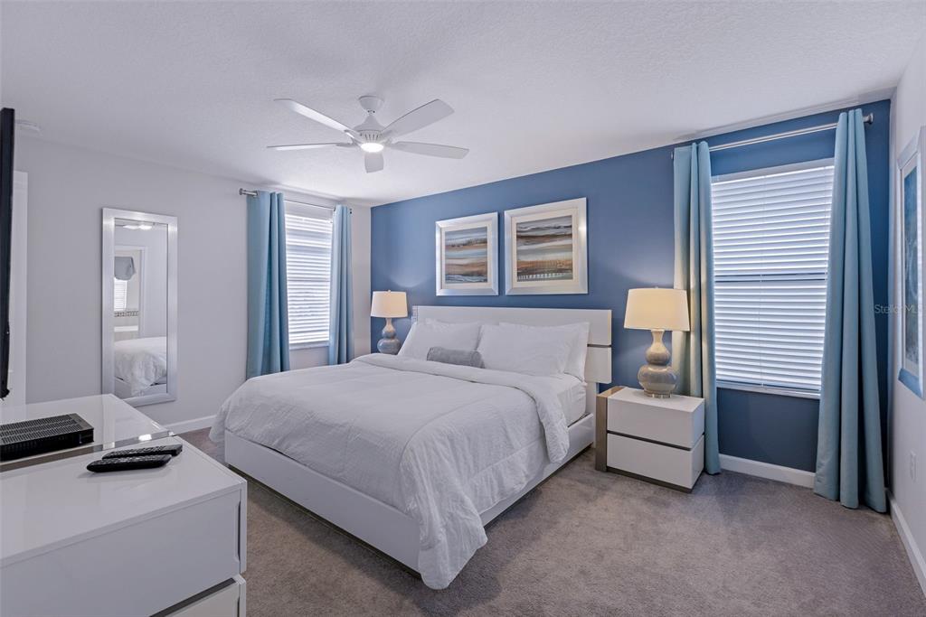 A bedroom features a white bed, blue accent wall, two nightstands, and light blue curtains — 9023 SHADOW MOUNTAIN STREET, DAVENPORT, FL